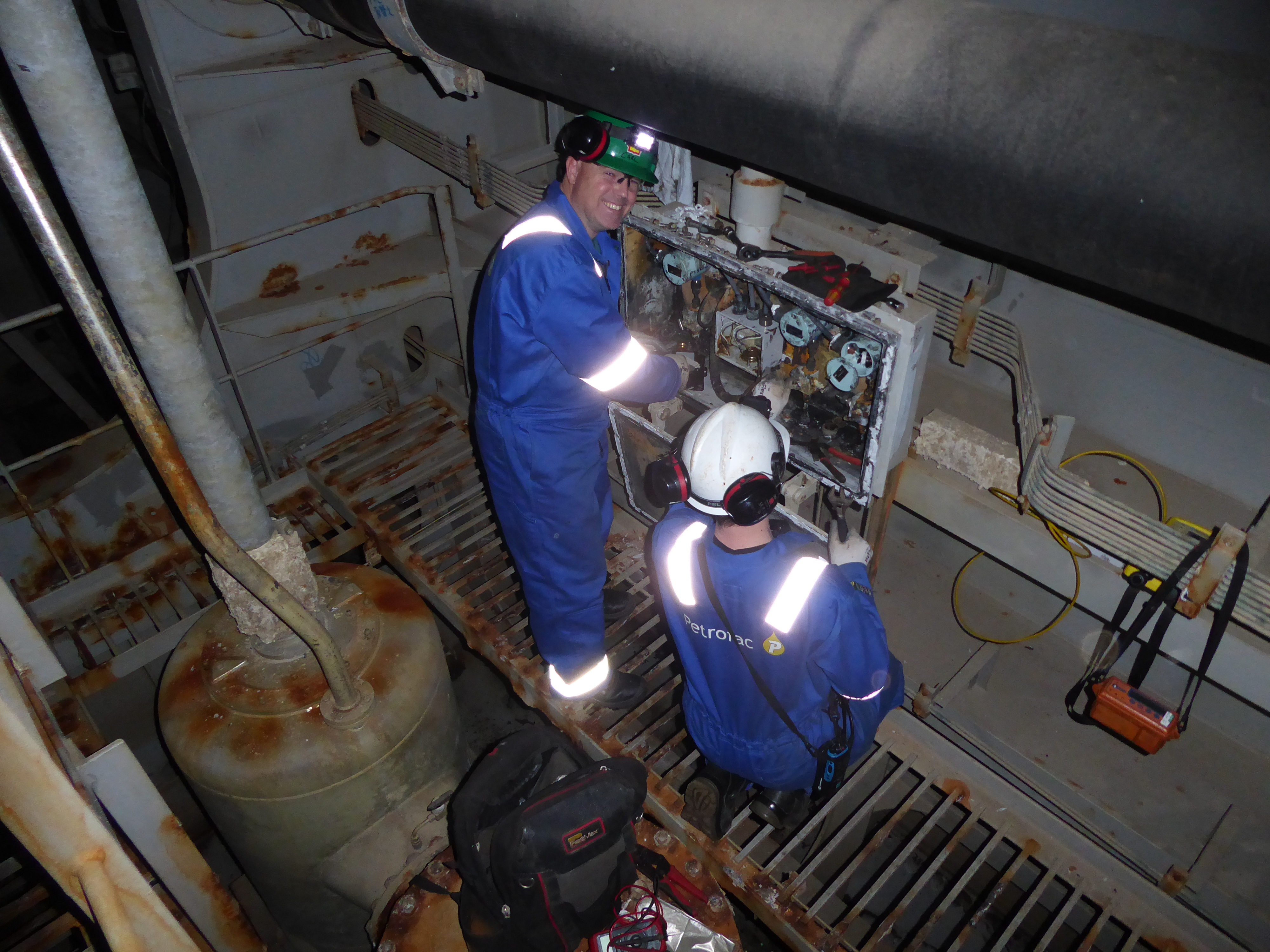 two electricians in a metal room looking at controls.